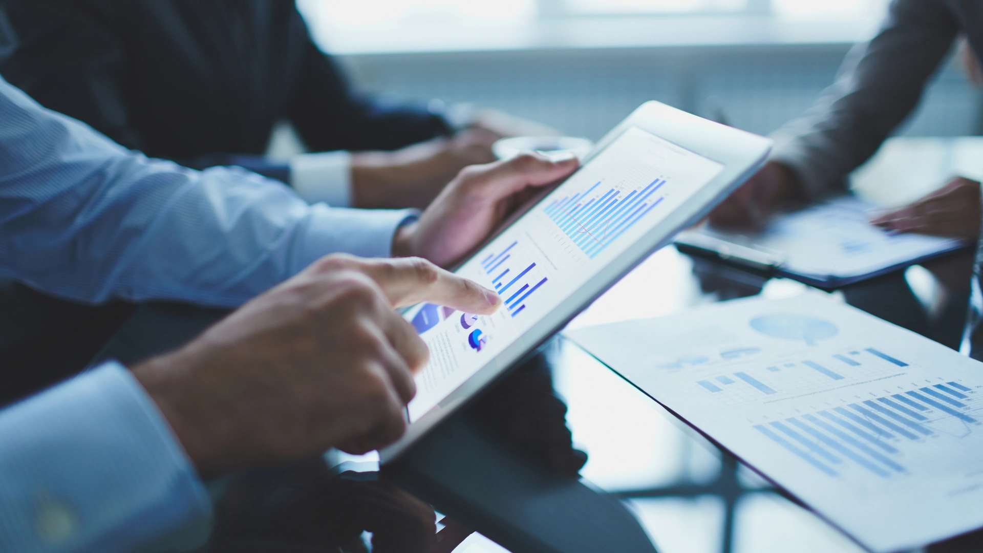 Hands pointing at a tablet displaying bar and pie charts during a financial review.